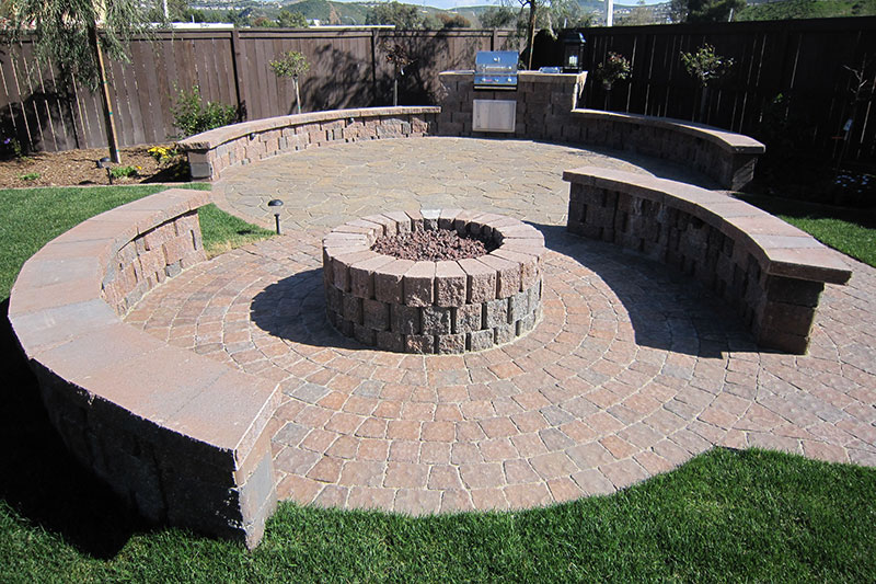 Outdoor firepit with stone seating, grill, and paver patio