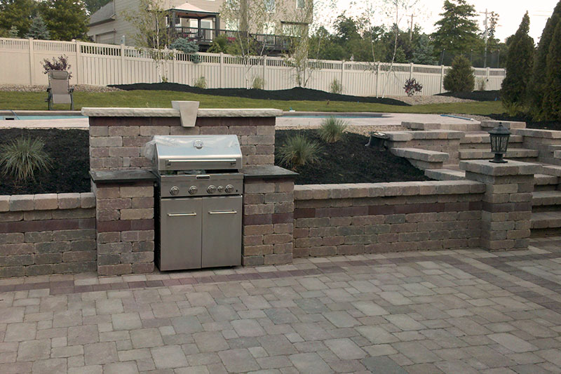 Outdoor kitchen with grill, counter, retaining wall, paver patio