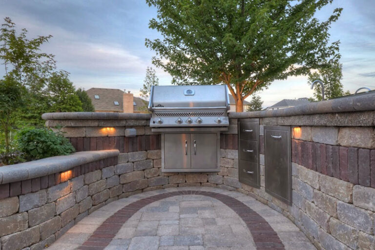 Outdoor kitchen with inlaid patio paver, grill, drawers, oven, stone seating